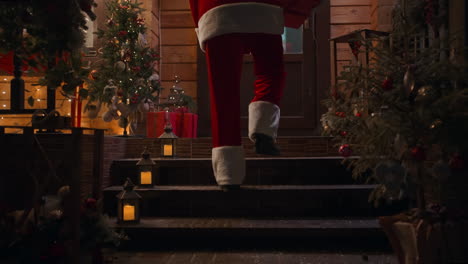 Nahaufnahme-Der-Füße-Des-Weihnachtsmanns,-Wie-Er-Die-Treppe-Hinaufsteigt-Und-Mit-Einem-Heiligabendgeschenk-Das-Haus-Betritt